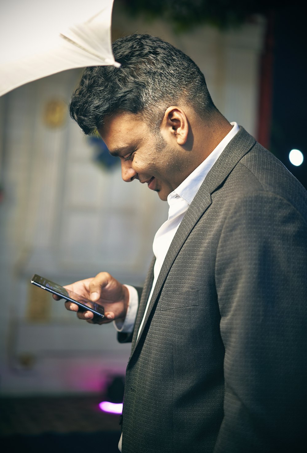A young man in a blazer smiling at his phone