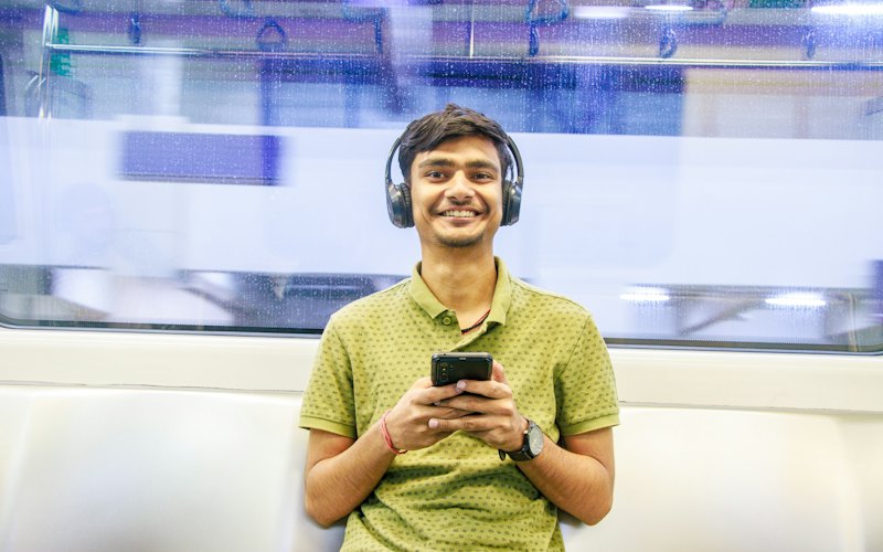 A young man with headphones smiling at his phone