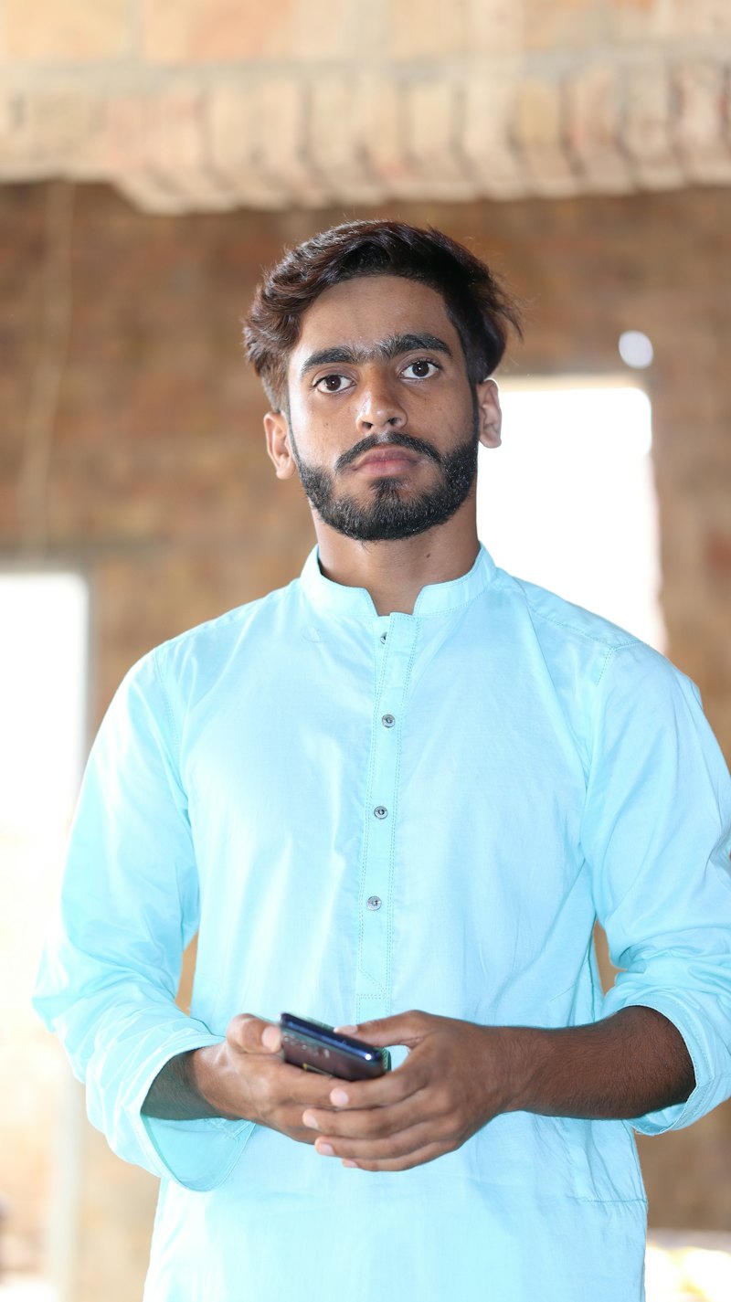 A young man in a light-blue kurta holding his phone